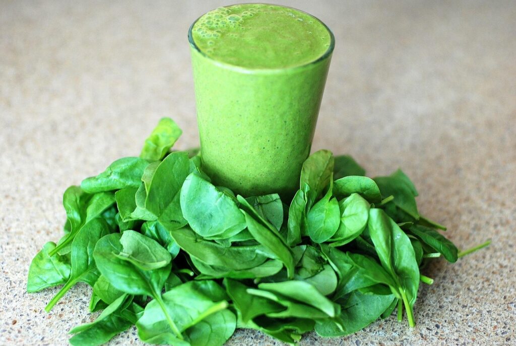 Vibrant green smoothie in a glass surrounded by fresh spinach leaves on a wooden surface, representing leafy greens for brain health and dementia prevention