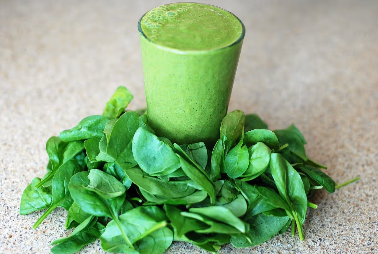 Vibrant green smoothie in a glass surrounded by fresh spinach leaves on a wooden surface, representing leafy greens for brain health and dementia prevention