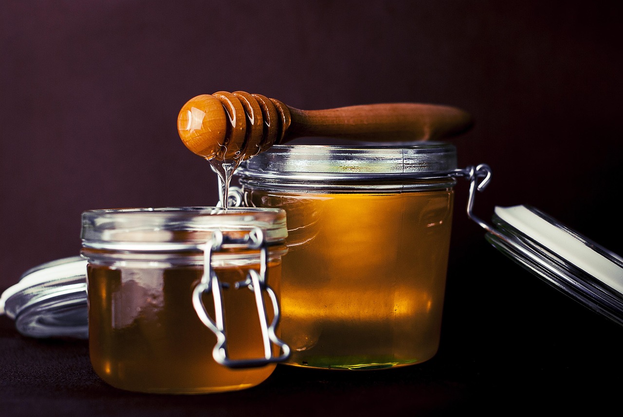 Glass jars of honey with a wooden honey dipper, representing natural honey for skin health, anti-aging, and UV protection benefits