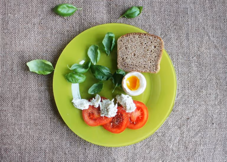 A healthy breakfast flat lay with a soft-boiled egg, sliced tomatoes, fresh basil, and toast on a plate, illustrating the best foods to pair with eggs for enhanced nutrition and nutrient synergy.
