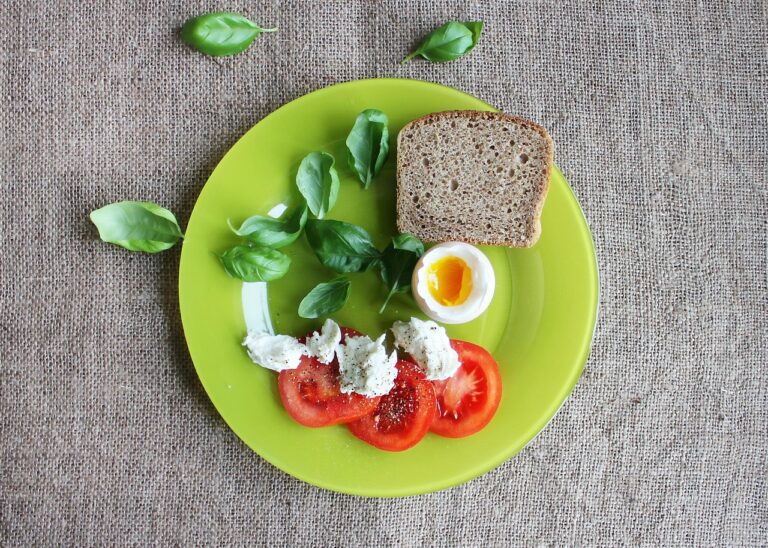 A healthy breakfast flat lay with a soft-boiled egg, sliced tomatoes, fresh basil, and toast on a plate, illustrating the best foods to pair with eggs for enhanced nutrition and nutrient synergy.