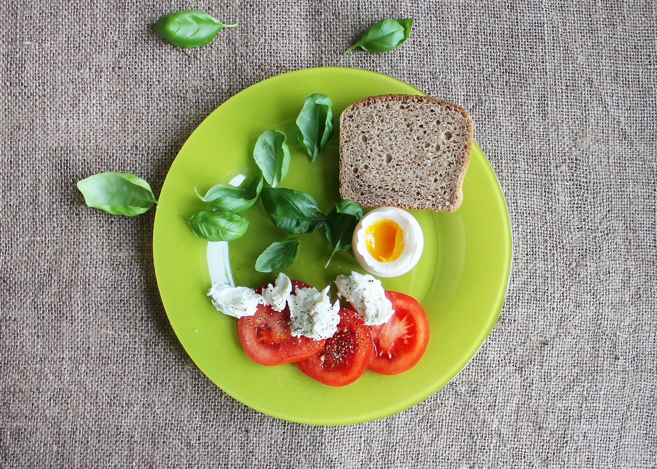 A healthy breakfast flat lay with a soft-boiled egg, sliced tomatoes, fresh basil, and toast on a plate, illustrating the best foods to pair with eggs for enhanced nutrition and nutrient synergy.