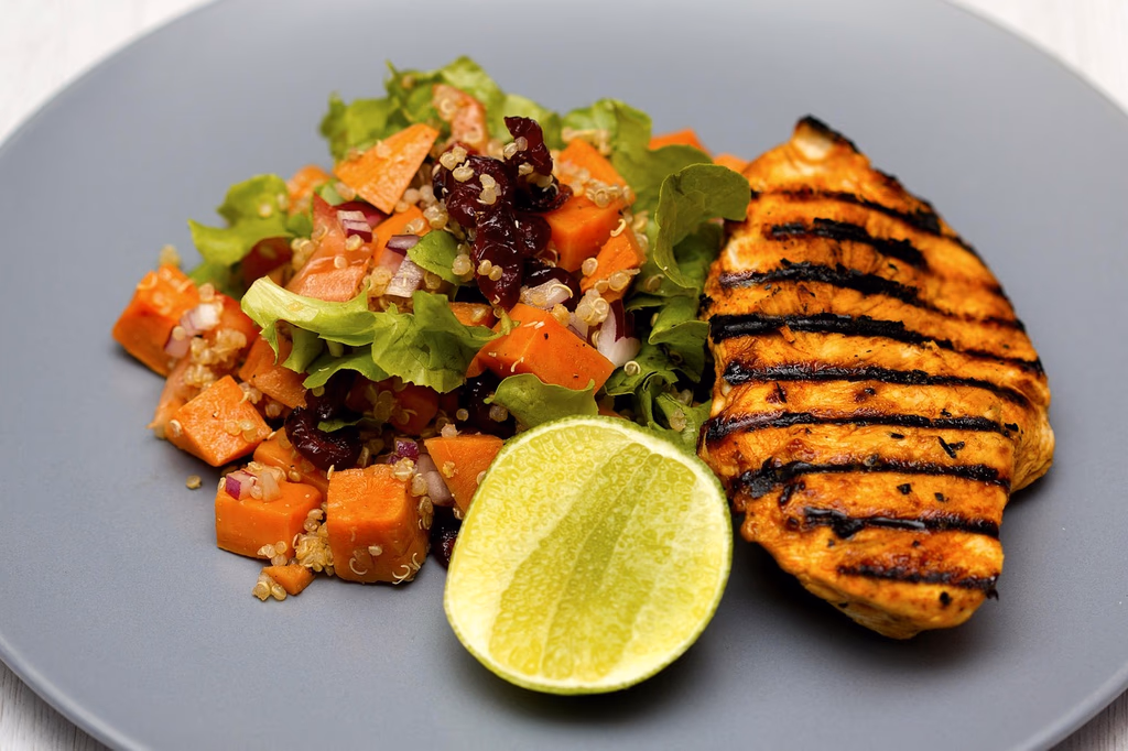 A healthy summer grain bowl featuring grilled chicken, quinoa, fresh vegetables, cherry tomatoes, and lemon, served on a plate for a nutritious 30-minute meal