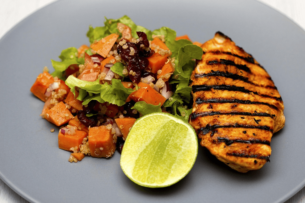 A healthy summer grain bowl featuring grilled chicken, quinoa, fresh vegetables, cherry tomatoes, and lemon, served on a plate for a nutritious 30-minute meal