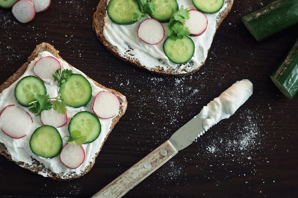 Cucumber toast topped with a creamy yogurt-herb spread and fresh radish slices on a wooden board, perfect for a healthy summer snack