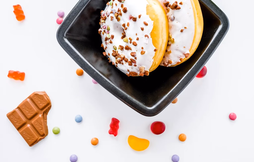 Assorted sugary treats including donuts, chocolate, and candies arranged on a dark surface, representing the high-sugar foods and beverages linked to negative brain health effects