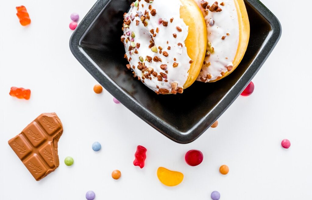 Assorted sugary treats including donuts, chocolate, and candies arranged on a dark surface, representing the high-sugar foods and beverages linked to negative brain health effects