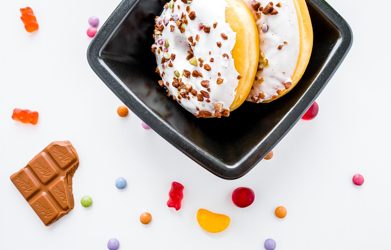 Assorted sugary treats including donuts, chocolate, and candies arranged on a dark surface, representing the high-sugar foods and beverages linked to negative brain health effects