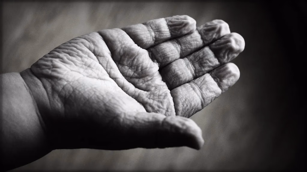 Close-up of two hands touching — one wrinkled aging hand and one younger hand — representing solo aging, connection, and the need for supportive care networks in later life.