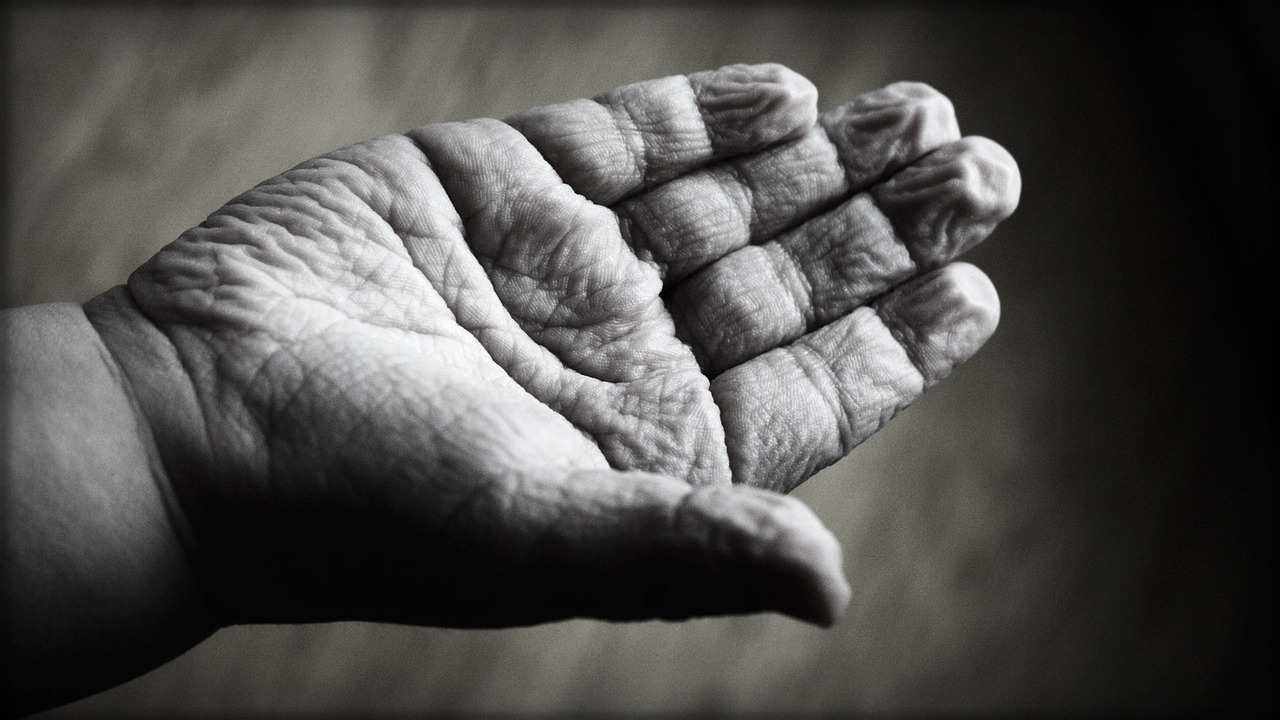 Close-up of two hands touching — one wrinkled aging hand and one younger hand — representing solo aging, connection, and the need for supportive care networks in later life.