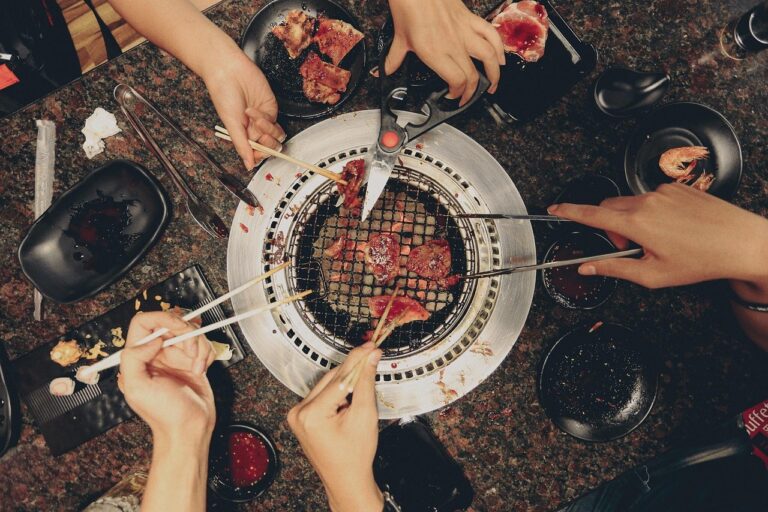 Group of friends enjoying a meal together around a grill outdoors, illustrating the social eating longevity habit of communal dining