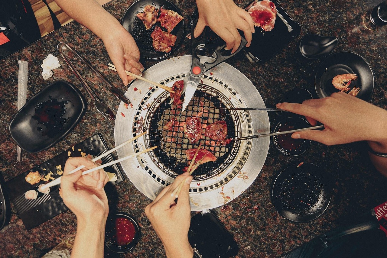 Group of friends enjoying a meal together around a grill outdoors, illustrating the social eating longevity habit of communal dining