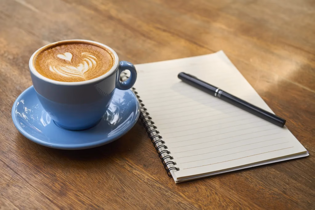 A cup of coffee with latte art on a table next to an open notebook and pen, representing the concept of pre-workout coffee as a natural performance booster for active women