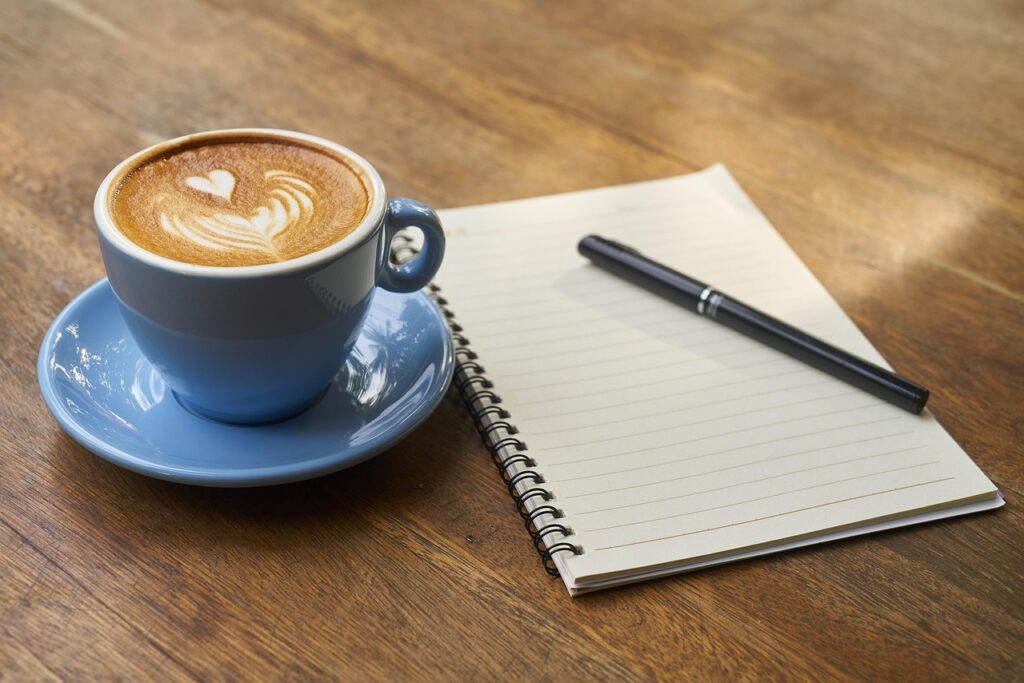 A cup of coffee with latte art on a table next to an open notebook and pen, representing the concept of pre-workout coffee as a natural performance booster for active women