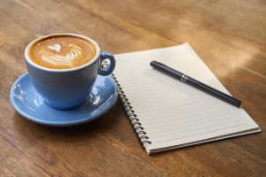 A cup of coffee with latte art on a table next to an open notebook and pen, representing the concept of pre-workout coffee as a natural performance booster for active women