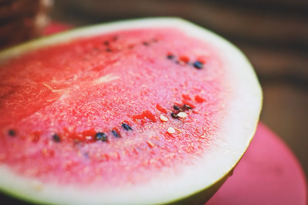 Close-up of a fresh watermelon slice showing vibrant red flesh, black seeds, and green rind on a wooden surface, illustrating healthy summer watermelon recipes for hydration and nutrition.