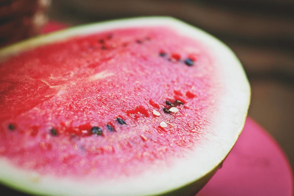 Close-up of a fresh watermelon slice showing vibrant red flesh, black seeds, and green rind on a wooden surface, illustrating healthy summer watermelon recipes for hydration and nutrition.