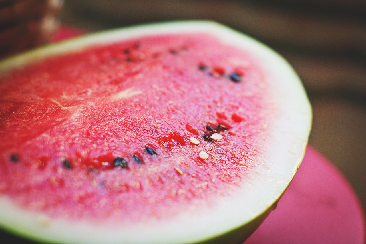 Close-up of a fresh watermelon slice showing vibrant red flesh, black seeds, and green rind on a wooden surface, illustrating healthy summer watermelon recipes for hydration and nutrition.