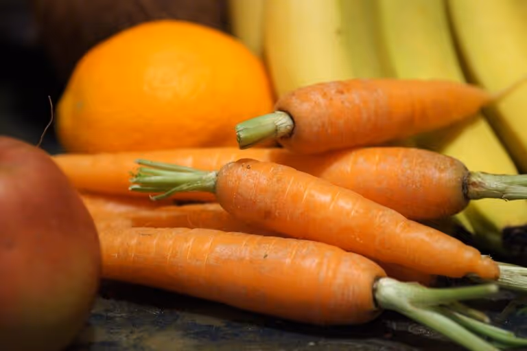 Colorful fresh fruits and vegetables including carrots, bananas, and apples arranged on a surface, representing natural vitamins and healthy nutrition for the best men's multivitamin buyer's guide