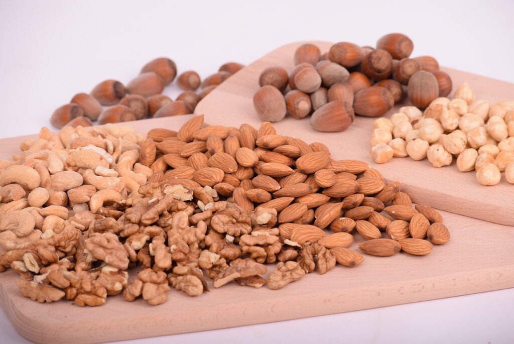 A variety of mixed nuts including almonds, walnuts, cashews, and hazelnuts on a wooden surface, representing healthy high-protein no-sugar snack options for summer