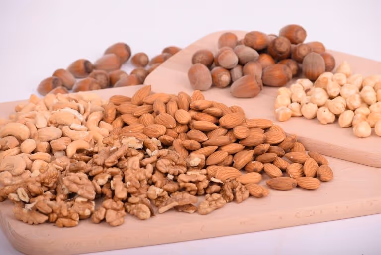 A variety of mixed nuts including almonds, walnuts, cashews, and hazelnuts on a wooden surface, representing healthy high-protein no-sugar snack options for summer