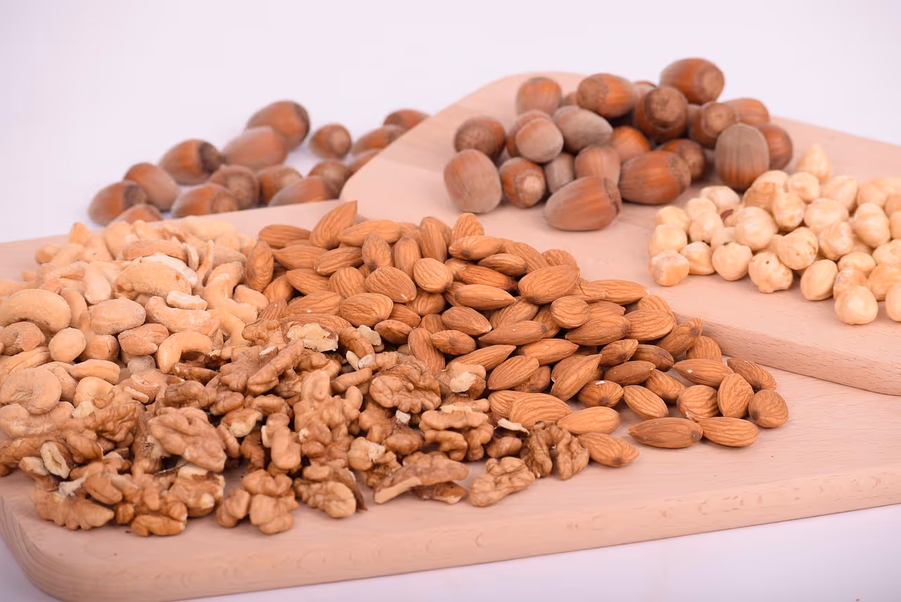 A variety of mixed nuts including almonds, walnuts, cashews, and hazelnuts on a wooden surface, representing healthy high-protein no-sugar snack options for summer
