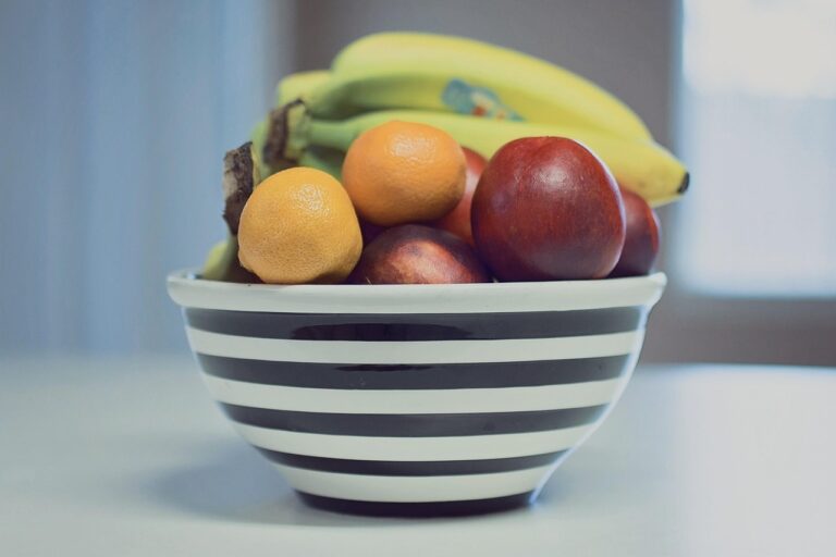 A colorful bowl of fresh summer fruit including strawberries, bananas, oranges, and apples on a white surface - ideal for summer breakfast recipes