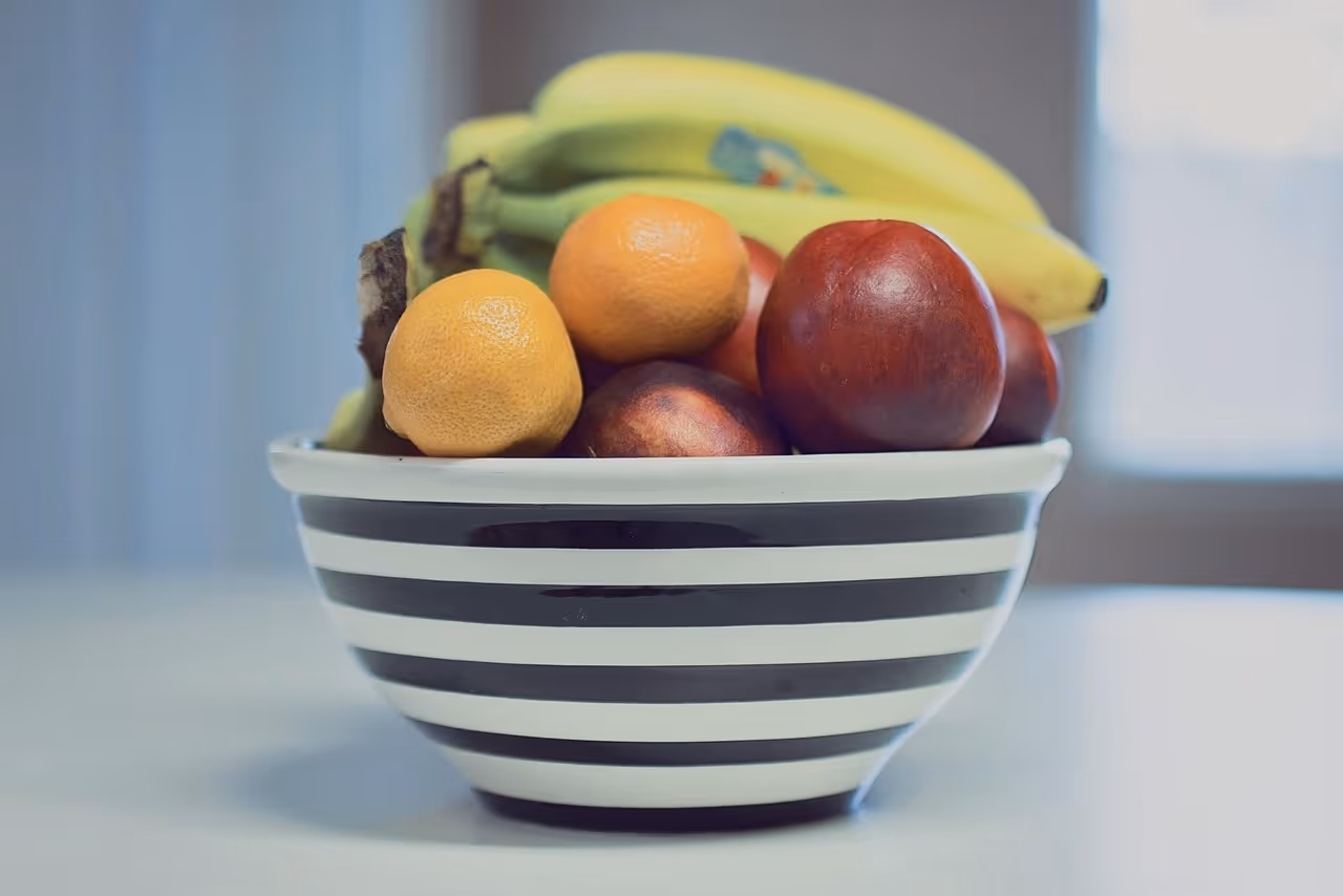 A colorful bowl of fresh summer fruit including strawberries, bananas, oranges, and apples on a white surface - ideal for summer breakfast recipes