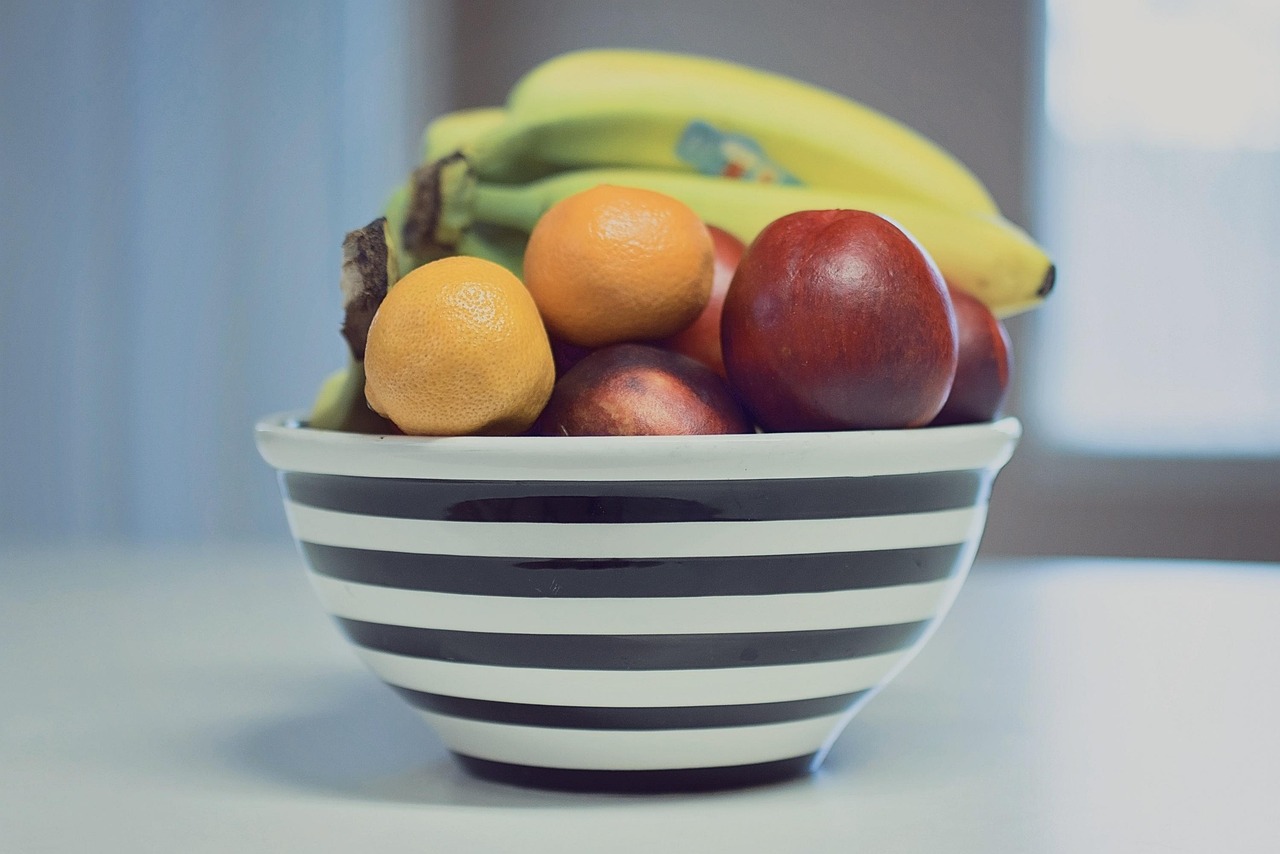 A colorful bowl of fresh summer fruit including strawberries, bananas, oranges, and apples on a white surface - ideal for summer breakfast recipes