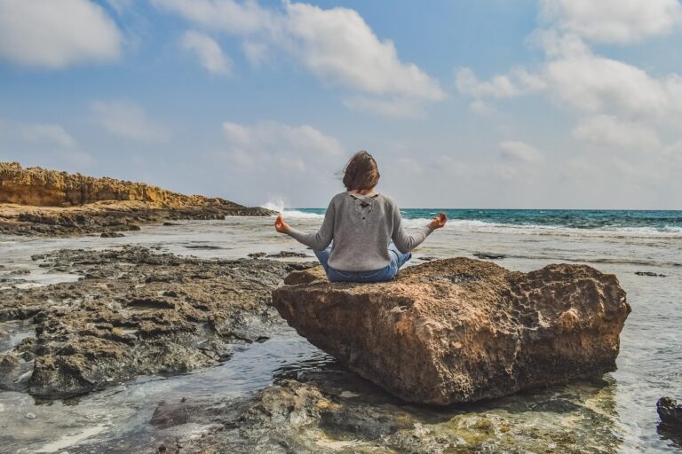 Woman sitting in meditation pose by the sea, representing a holistic and calming approach to managing PCOS high testosterone and hormone health