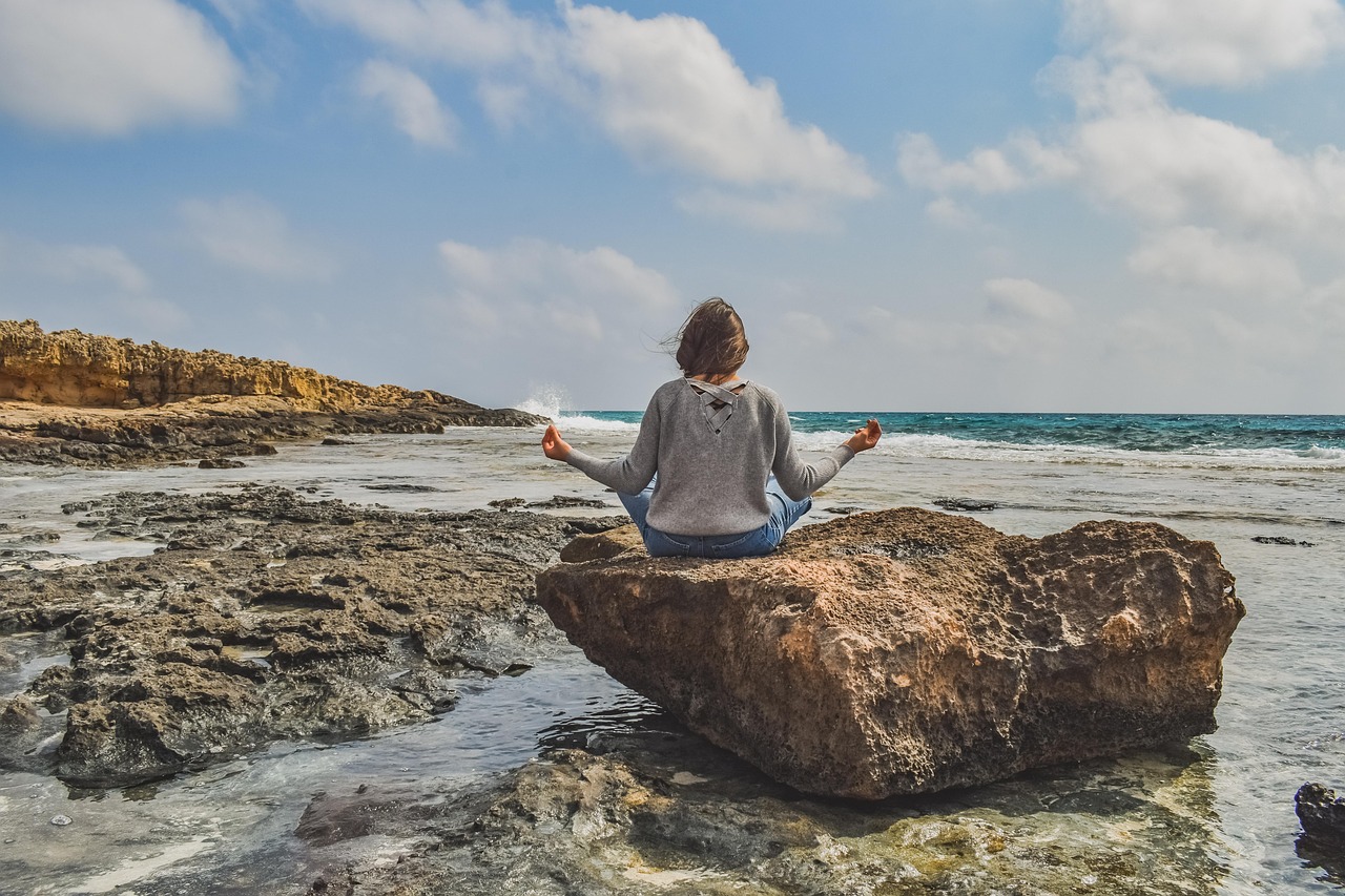 Woman sitting in meditation pose by the sea, representing a holistic and calming approach to managing PCOS high testosterone and hormone health