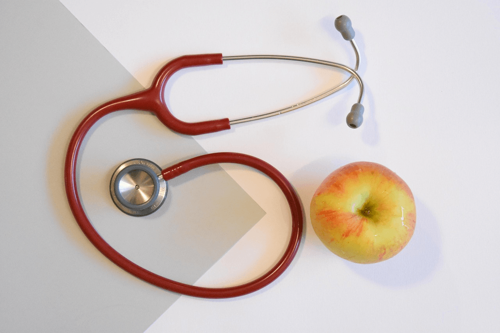 A stethoscope placed beside a red apple on a wooden surface, symbolizing heart disease prevention through healthy eating and medical care