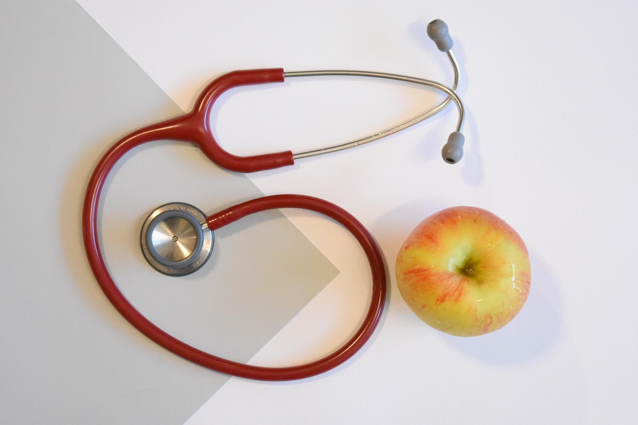 A stethoscope placed beside a red apple on a wooden surface, symbolizing heart disease prevention through healthy eating and medical care