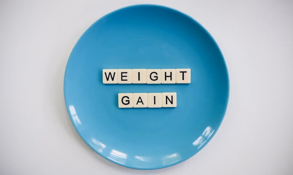 Scrabble tiles spelling out WEIGHT GAIN on a blue plate, representing the connection between sleep loss and weight gain from a 2026 study.