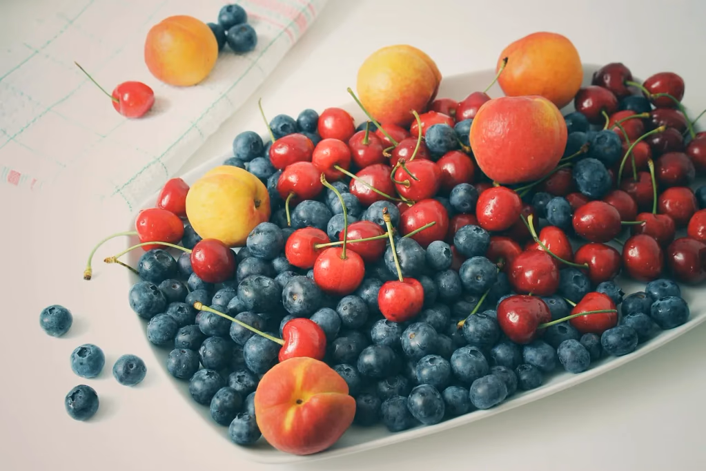 Vibrant summer fruit salad featuring fresh blueberries, apricots, and cherries arranged on a light surface, perfect for healthy summer potluck recipes