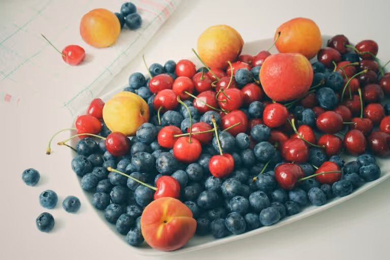 Vibrant summer fruit salad featuring fresh blueberries, apricots, and cherries arranged on a light surface, perfect for healthy summer potluck recipes