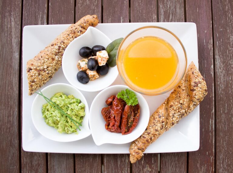 A healthy breakfast table spread featuring avocado slices, whole-grain bread, olives, sun-dried tomatoes, and orange juice on a wooden table - perfect example of a quick balanced breakfast with protein, fiber, and healthy fats