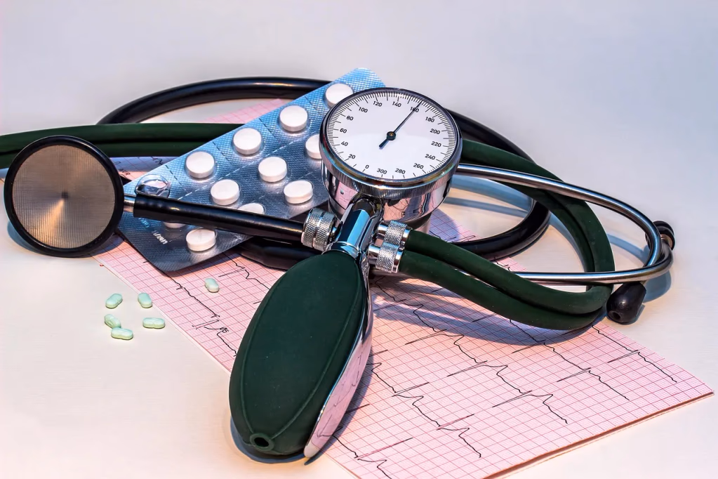 Blood pressure monitor, stethoscope, and ECG heart rhythm chart on a table with medication, representing tools for monitoring evening blood pressure and hypertension management