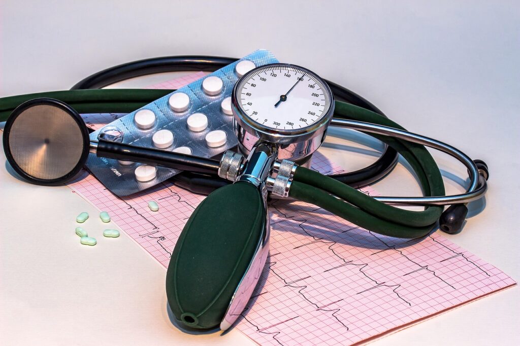 Blood pressure monitor, stethoscope, and ECG heart rhythm chart on a table with medication, representing tools for monitoring evening blood pressure and hypertension management