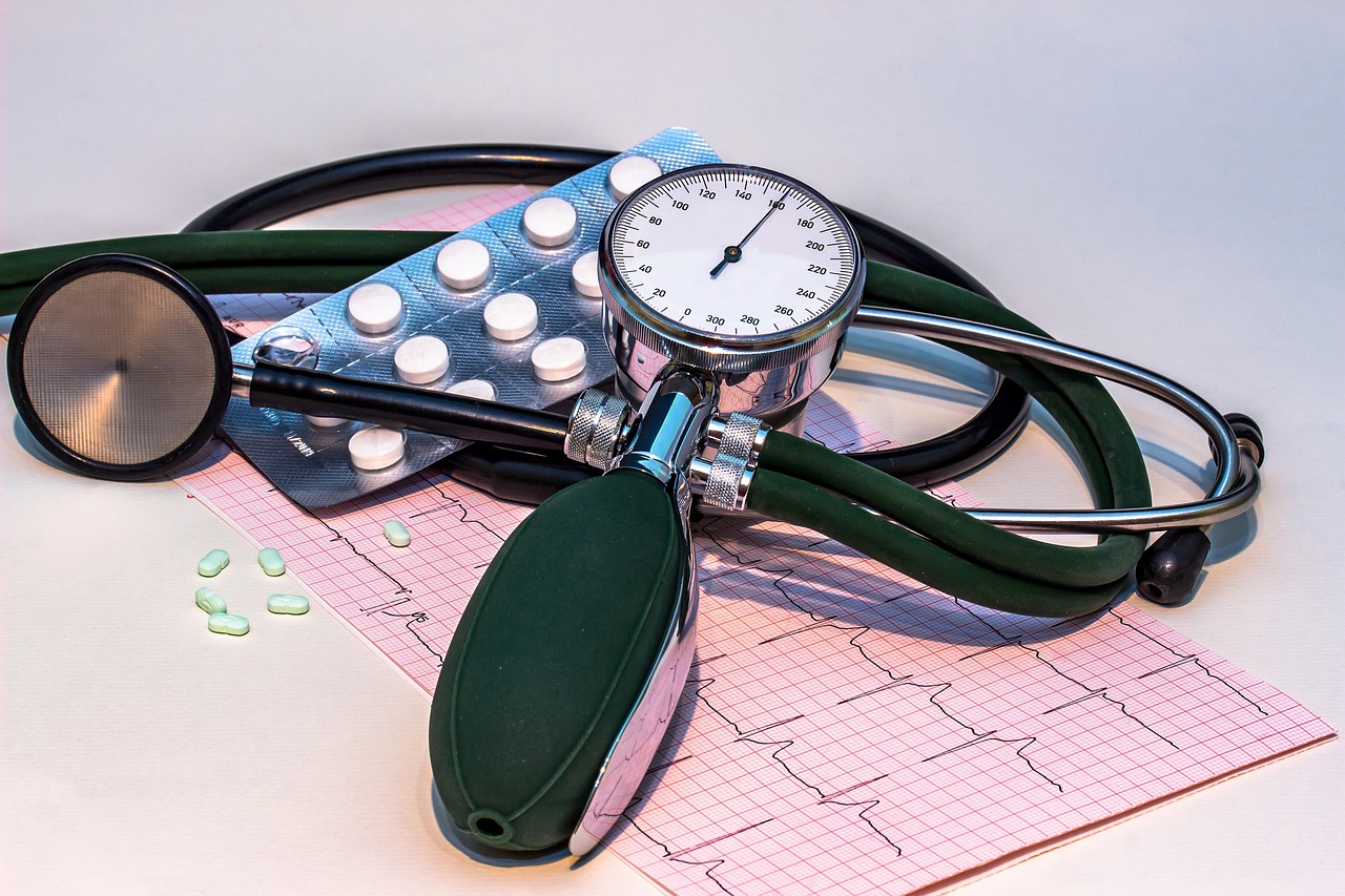Blood pressure monitor, stethoscope, and ECG heart rhythm chart on a table with medication, representing tools for monitoring evening blood pressure and hypertension management