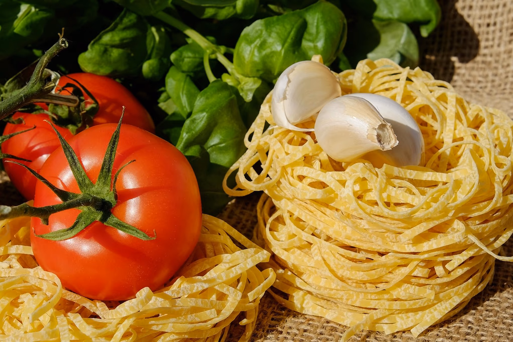 Fresh pasta noodles with cherry tomatoes, basil leaves, and garlic cloves on a wooden table - ingredients for Ina Garten's Summer Garden Pasta recipe