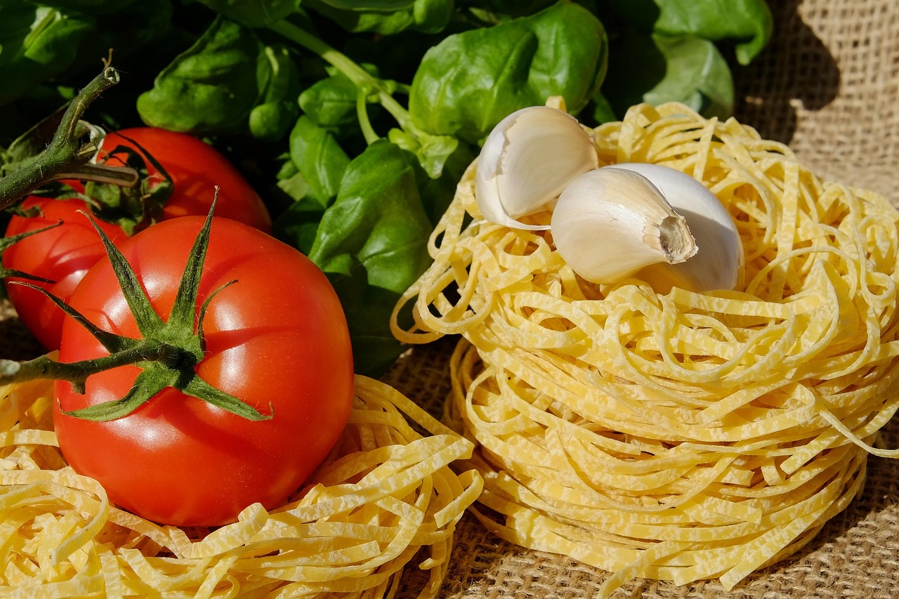 Fresh pasta noodles with cherry tomatoes, basil leaves, and garlic cloves on a wooden table - ingredients for Ina Garten's Summer Garden Pasta recipe