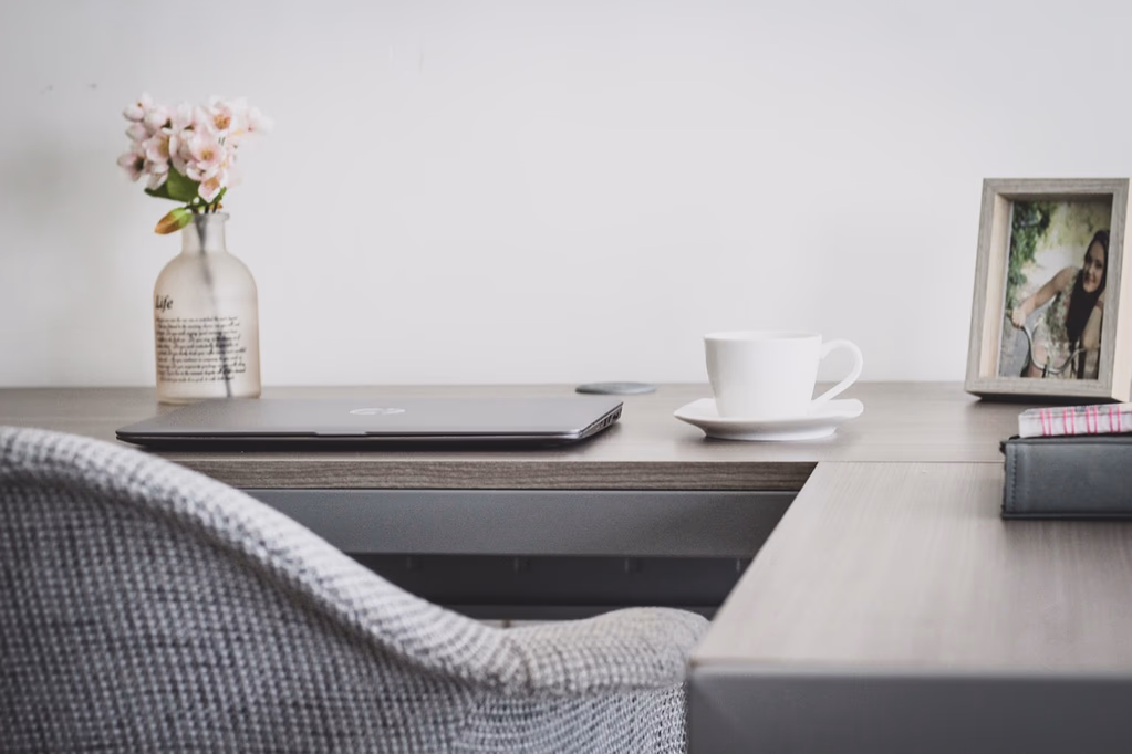 A clean, organized home office workspace with a laptop, coffee cup, and small plant on a wooden desk, representing a calm and productive work environment