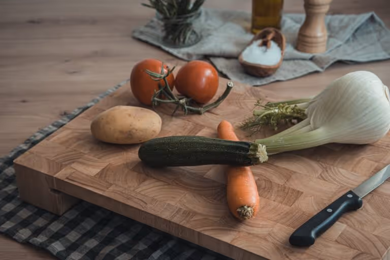 Fresh vegetables being prepared on a wooden cutting board with olive oil and herbs, representing a healthy, plastic-free kitchen