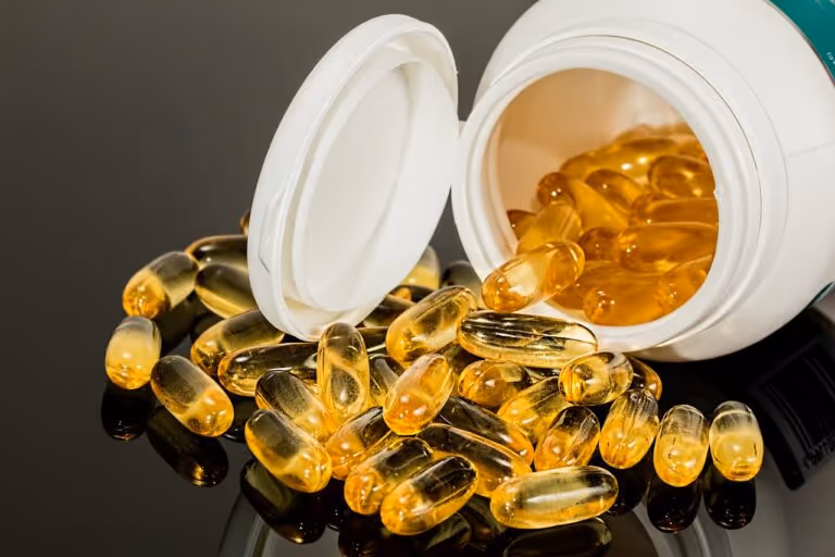 Omega-3 fish oil supplement capsules in translucent golden and white colors spilling from a glass bottle on a white surface, representing omega-3 supplementation for heart and brain health