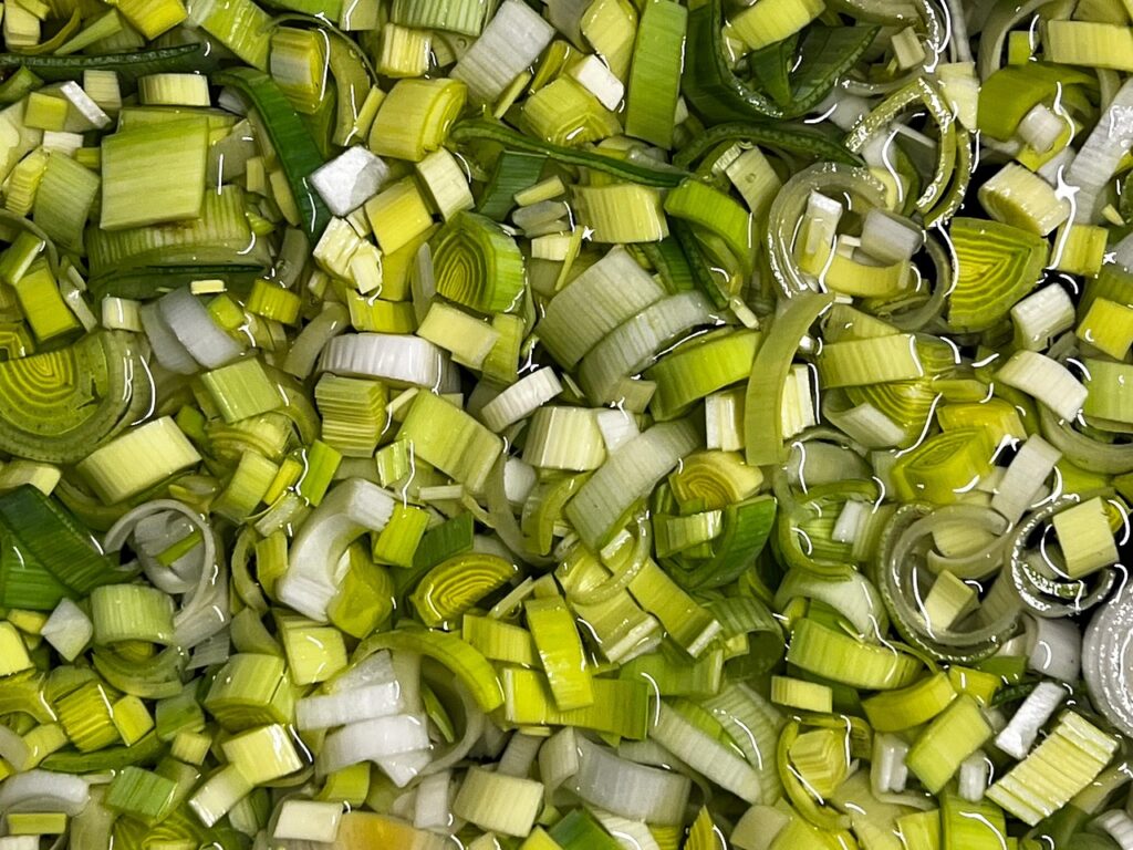 Fresh leek being washed under running water in a kitchen sink, demonstrating proper produce washing technique for cyclosporiasis prevention and food safety