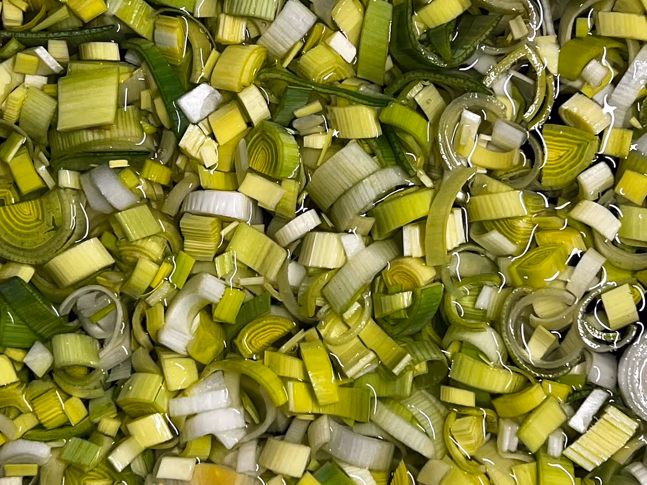 Fresh leek being washed under running water in a kitchen sink, demonstrating proper produce washing technique for cyclosporiasis prevention and food safety