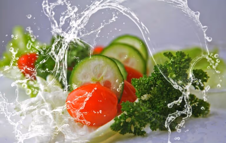 Fresh salad of cucumbers, tomatoes, and green leaves splashing with water droplets, representing hydrating salads for summer hydration