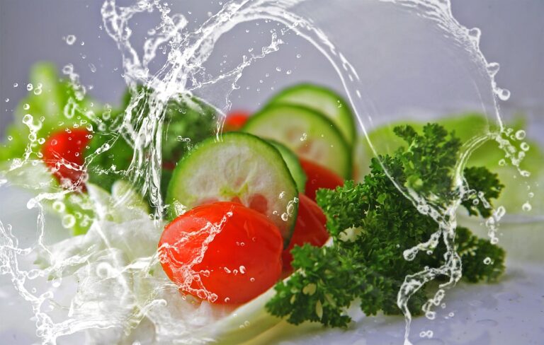 Fresh salad of cucumbers, tomatoes, and green leaves splashing with water droplets, representing hydrating salads for summer hydration