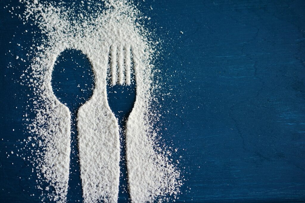 Powdered sugar silhouettes of a spoon and fork on a dark background, representing cutting out added sugar from lunch meals for weight loss